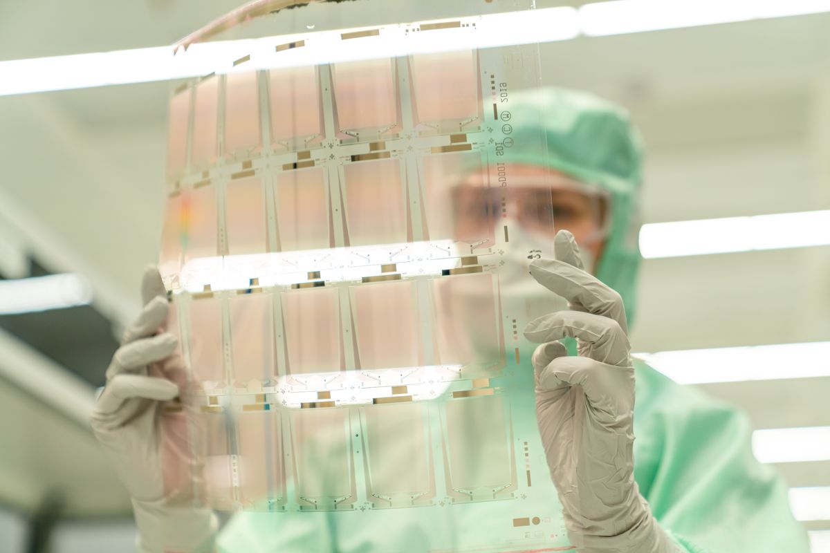 A scientist in protective gear holding a transparent test sheet in a laboratory